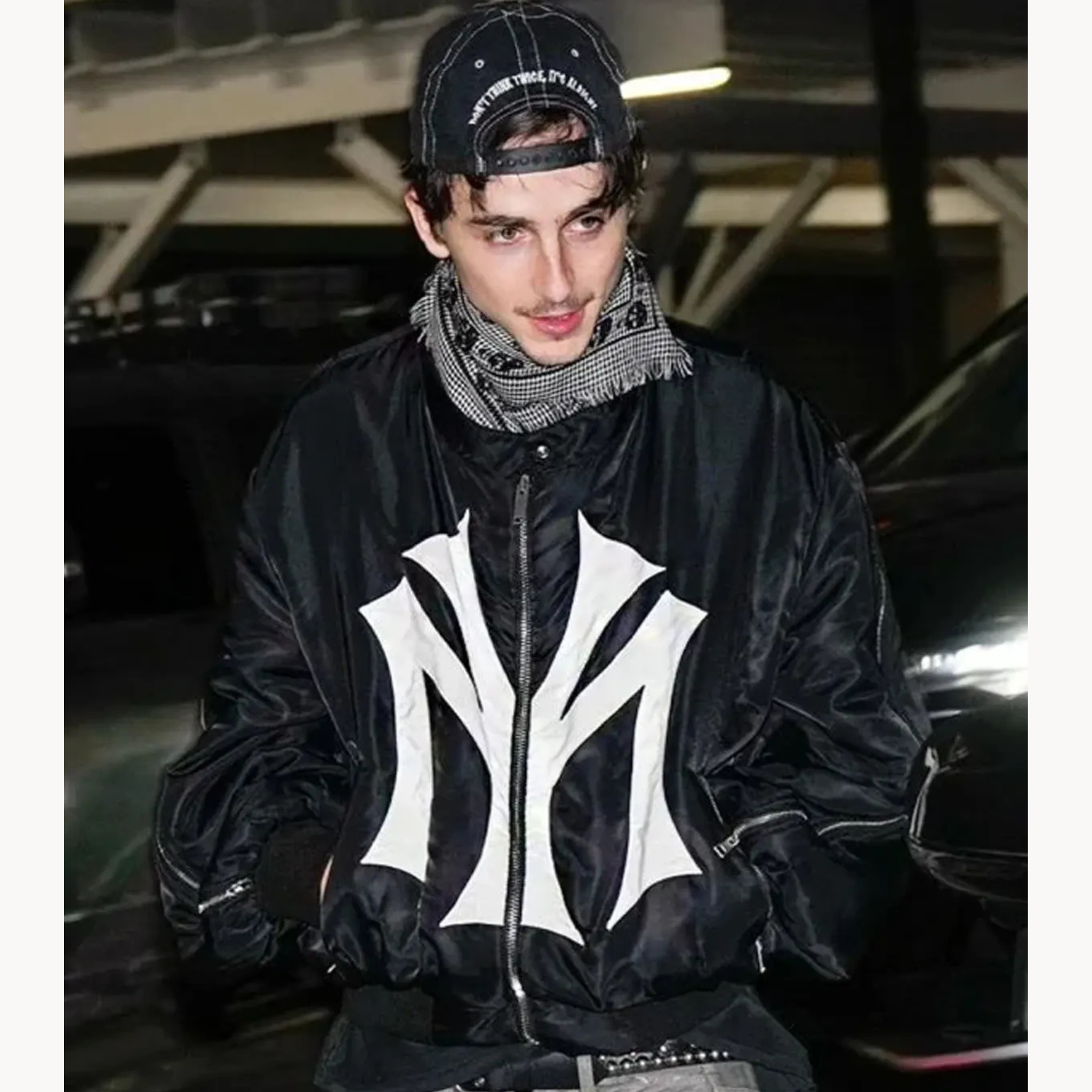 Timothée Chalamet wearing a My City Front NY logo print oversized black cropped bomber jacket with sleeve zippers.